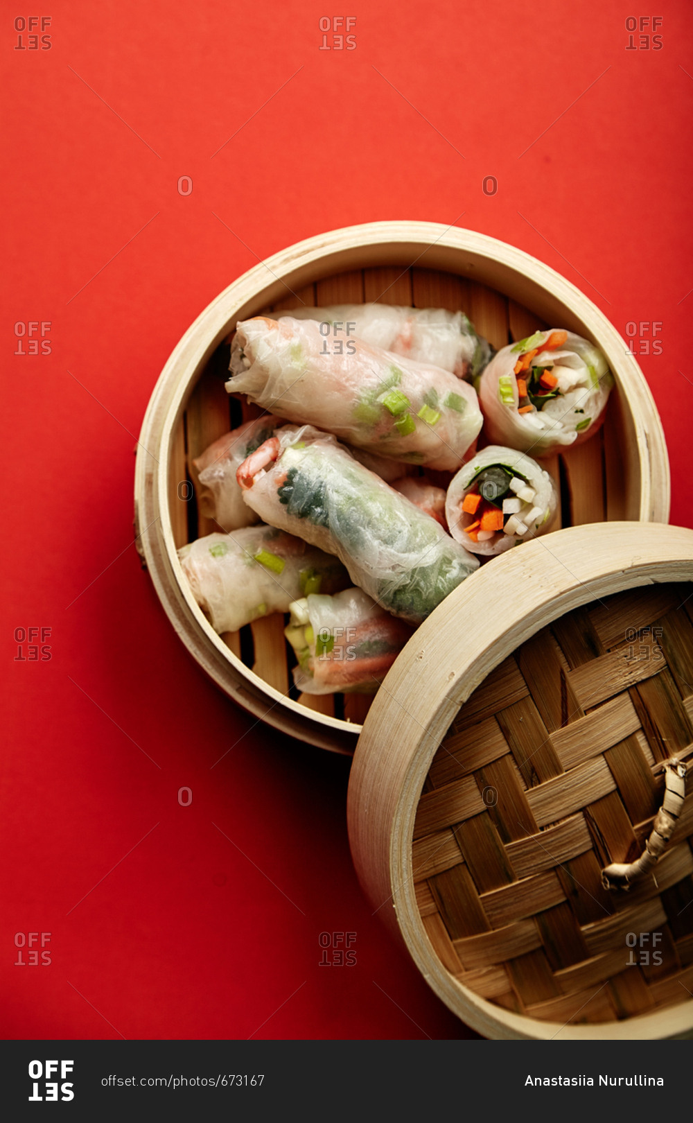 Spring rolls with shrimps and marinated vegetables in bamboo steamer on red background