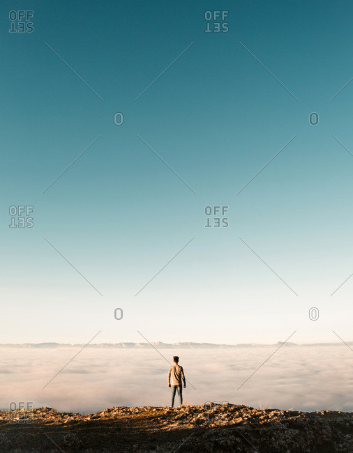 Back view of tourist standing at cliff edge over the clouds.