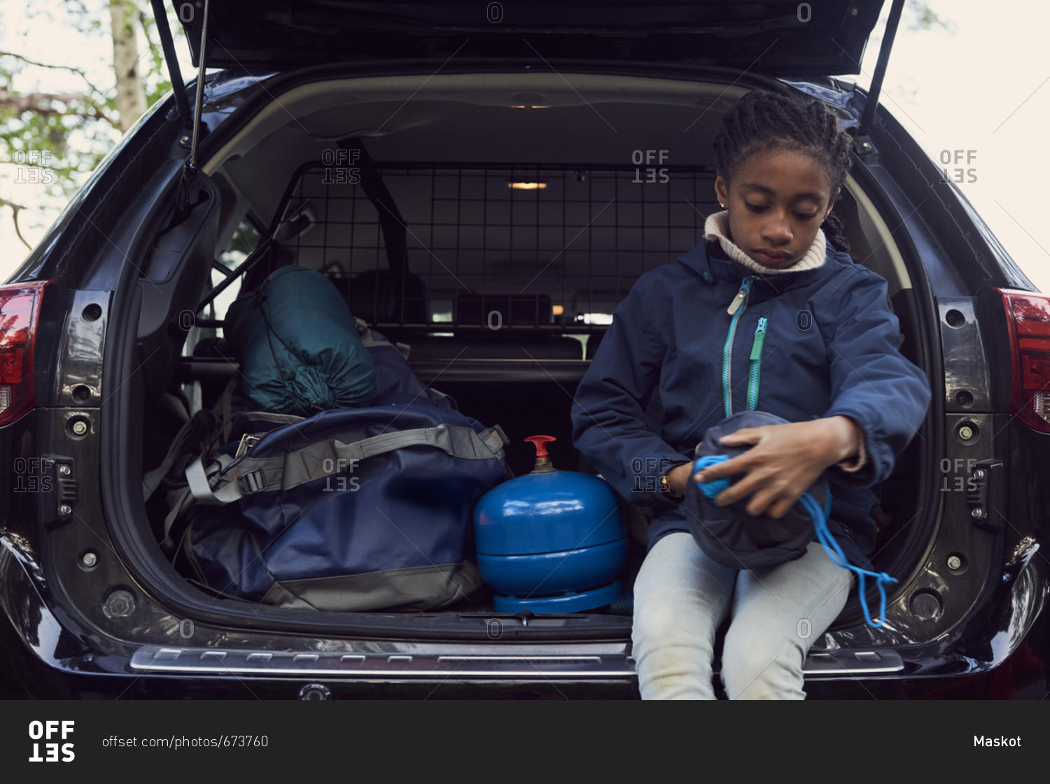 Girl sitting with camping gear in car trunk