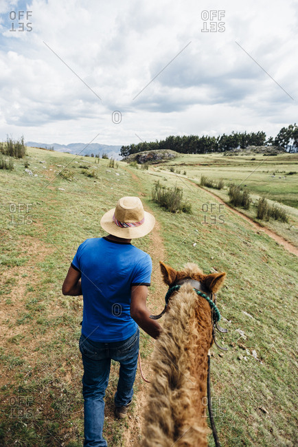 Cuzco, Peru - November 21, 2017: Inca man in hat with horse from behind and above against landscape