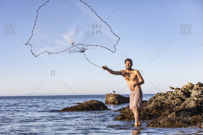Young man throwing fishing net in sea while standing by rock