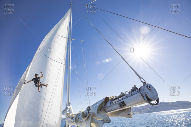 Man climbing the mast of a sailboat on a sunny day