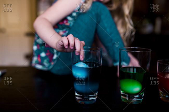 Girl touching an Easter egg while dying it blue