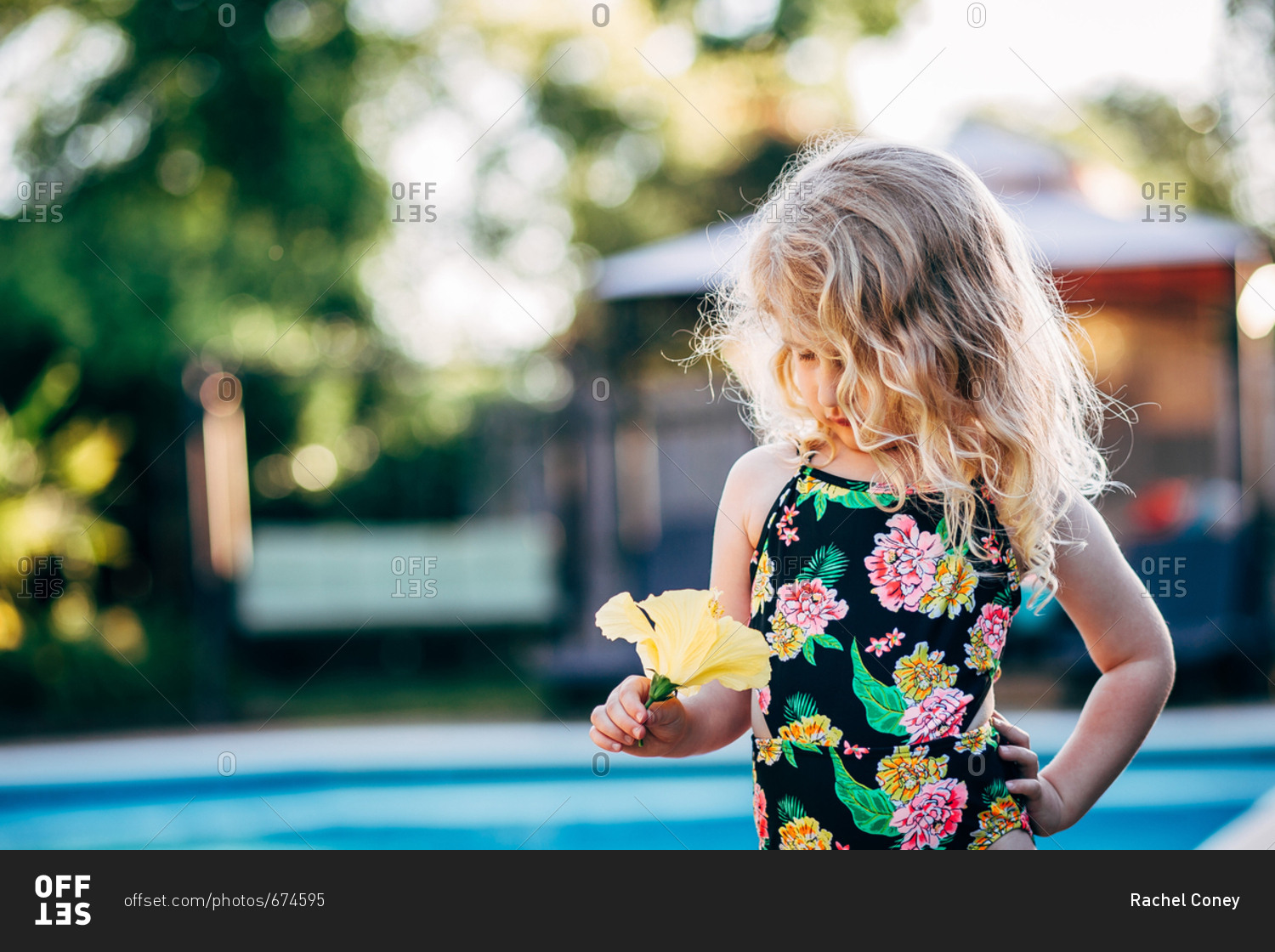 Little blonde girl holding yellow flower beside pool