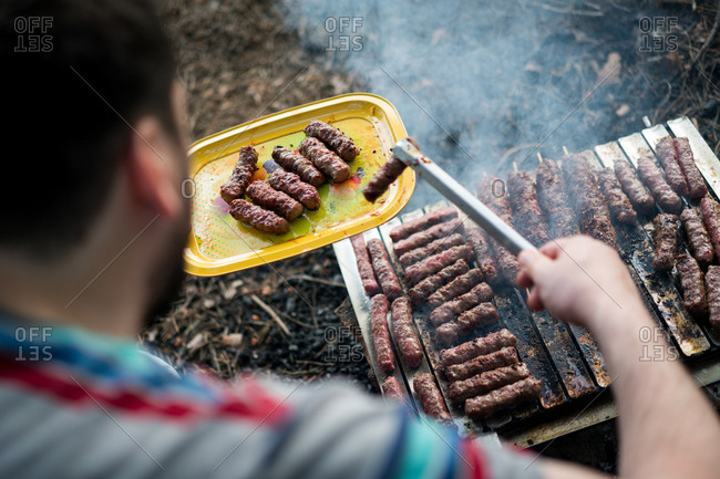 Man grilling sausage on a campfire grill