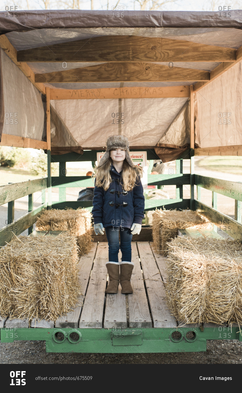 Full length of girl standing on vehicle trailer by hay bales at farm