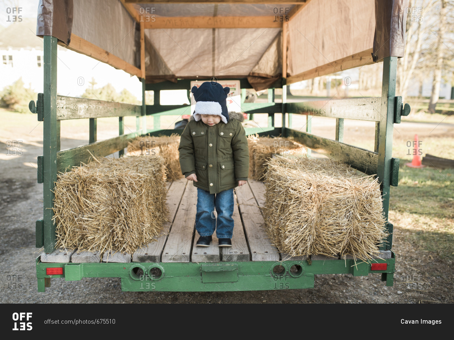 Full length of boy standing on vehicle trailer by hay bales at farm