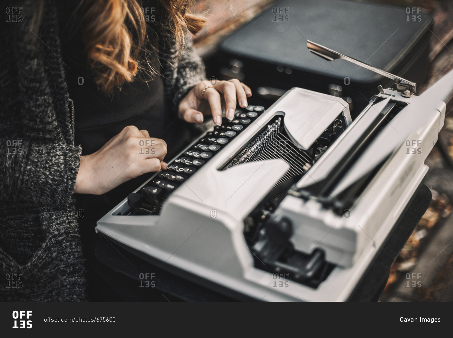 Midsection of female writer using typewriter while sitting on bench at park