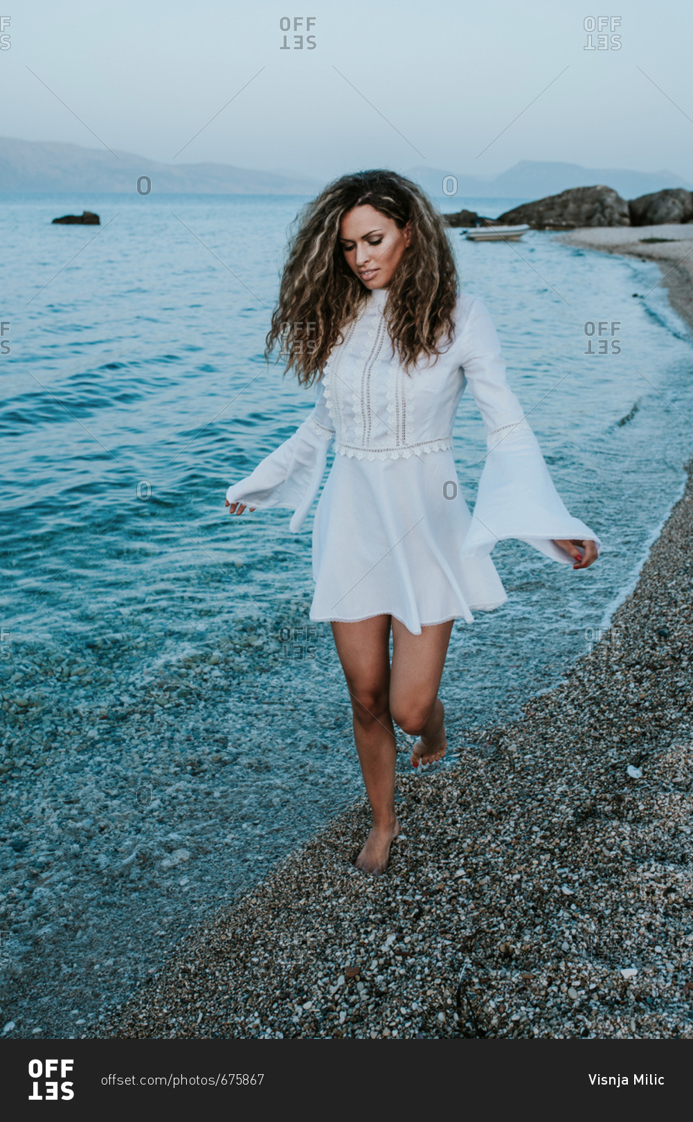 Portrait of girl with long curly hair in white summer dress on the beach at the sea
