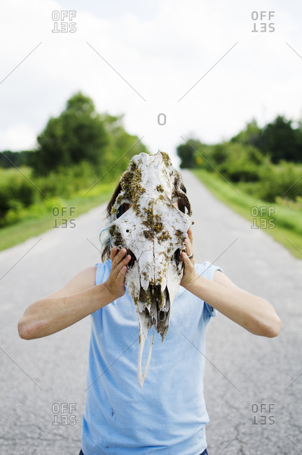 Young woman on country road wearing a moose skull as a mask