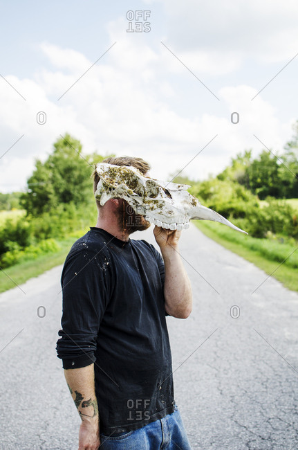 Young man on country road wearing a moose skull as a mask