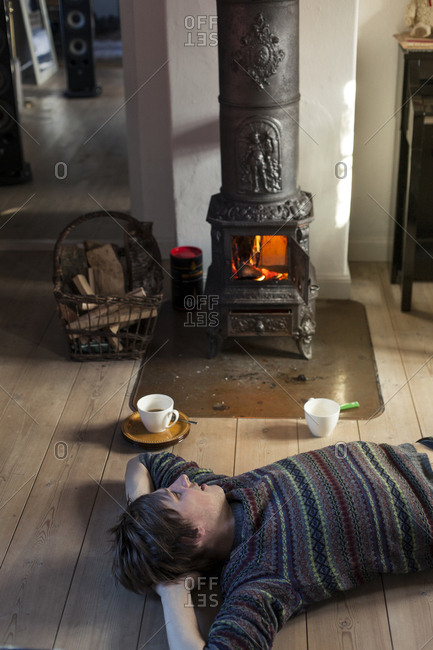 Person lying on floor with hot beverage next to wood-burning stove in  cottage stock photo - OFFSET