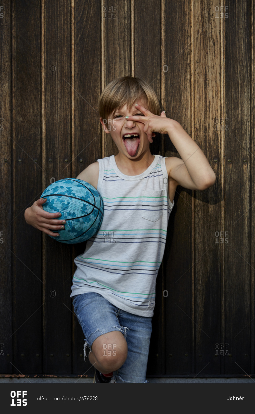 Portrait of boy holding ball and sticking tongue out