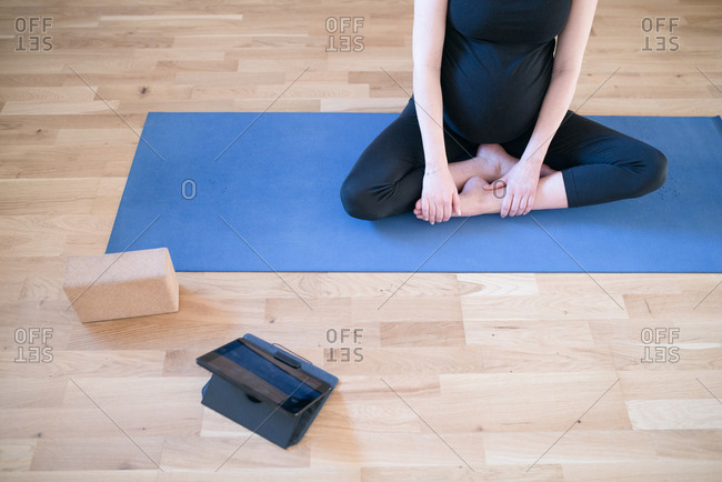 Pregnant woman sitting cross legged looking at tablet computer during yoga session