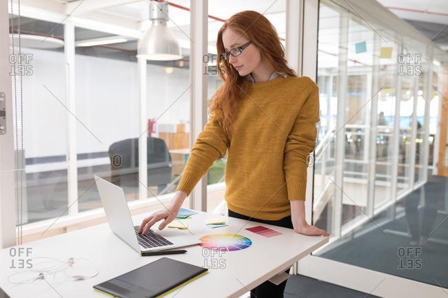 Young female graphic designer using laptop in office stock photo - OFFSET
