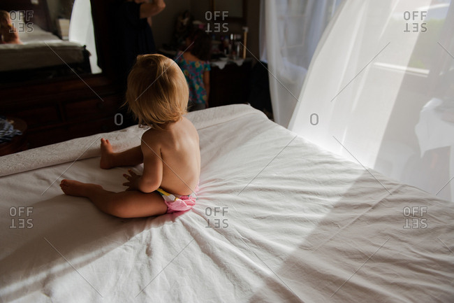 Little girl waking up from nap as breeze blows curtain