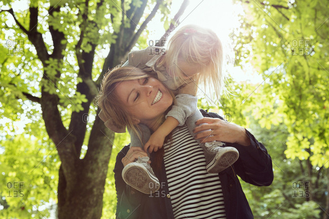 Mother giving toddler daughter shoulder carry in sunlit park