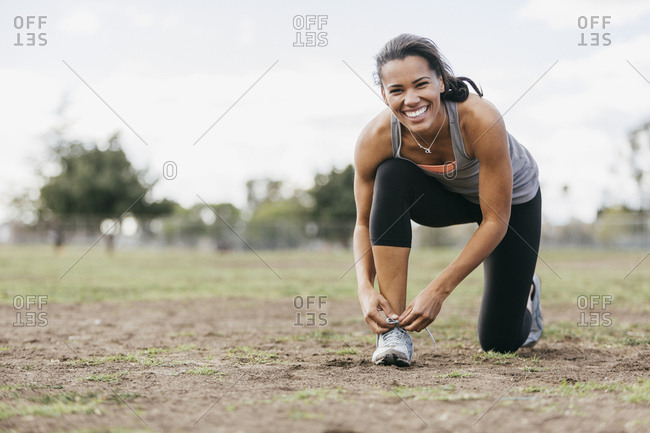 Young woman tying shoelace on field during workout at park