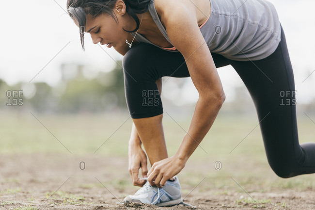 Sporty young woman tying shoelace on field during workout at park