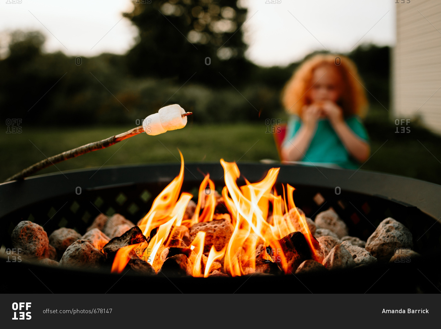 Marshmallow roasting over fire pit in front of little boy eating s\'more