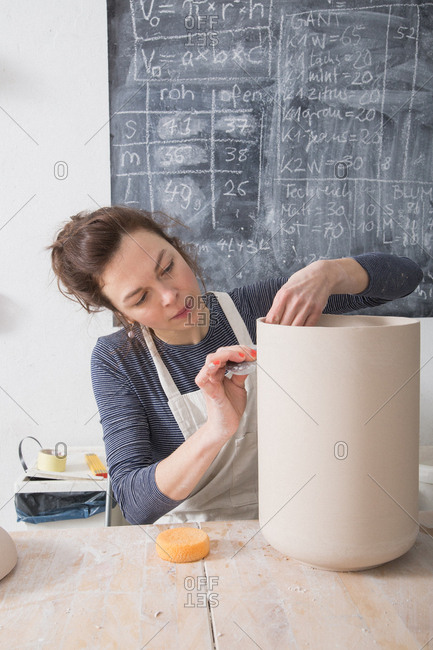 A ceremic artist is putting the finishing touches to a ceramic urn in a ceramic workshop.