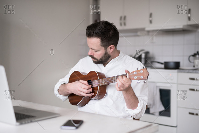 Businessman playing ukulele while seated at table in front of laptop computer
