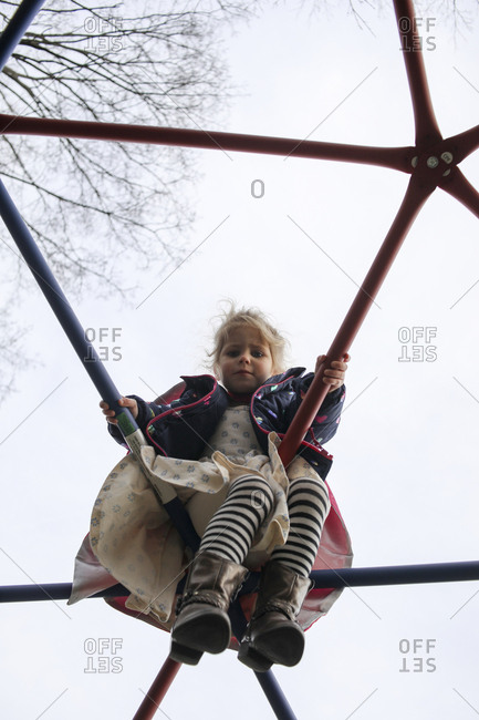Low angle portrait of cute girl sitting on jungle gym against clear sky at playground