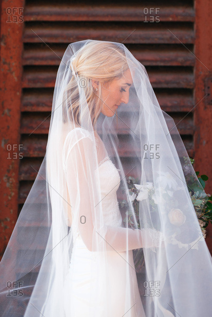 Profile view of bride waiting with bouquet and veil over head