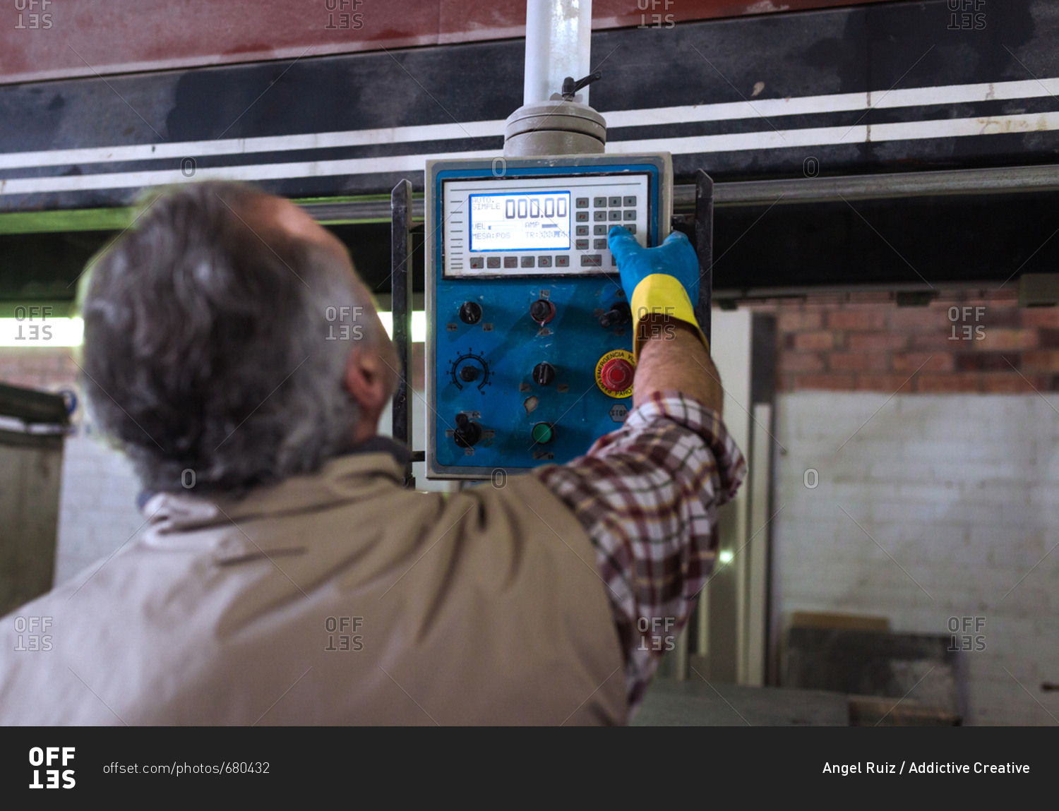 Back view of adult operator using control panel on machine on a factory.