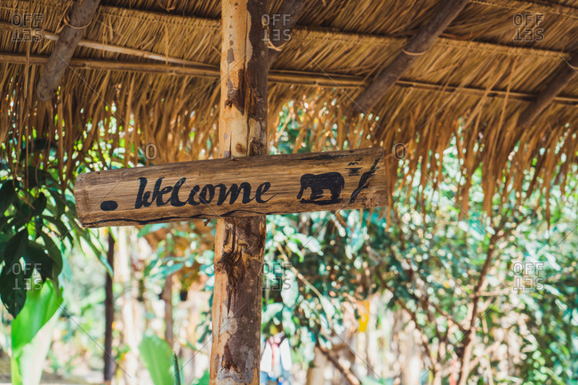 Wooden welcome sign with black elephant drawn under straw roof.