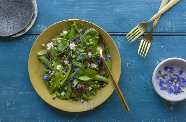 Green salad with peas, feta and edible flowers in a bowl with a serving spoon