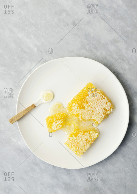Honeycomb with honey seeping out on a plate with a spoon on marble