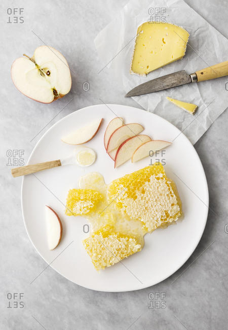 Honeycomb with apples and hard cheese on a plate on marble