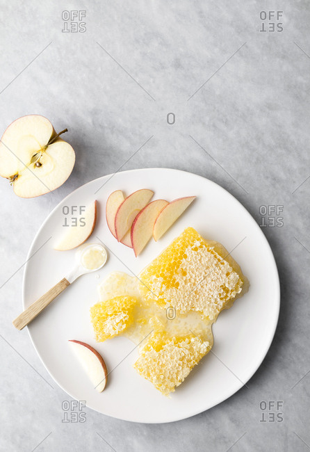 Honeycomb with apples and a spoonful of honey on a plate on marble