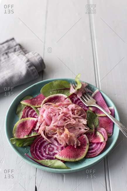A pink salad of beets, watermelon radishes, beet greens and sauerkraut on an aqua plate with a fork