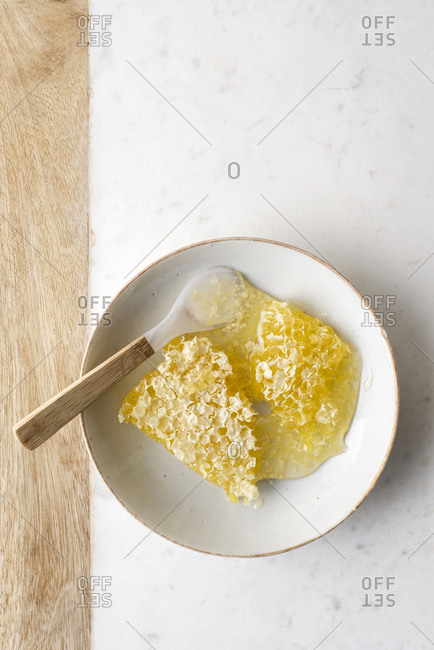 Honeycomb in a bowl with a spoon on a marble slab