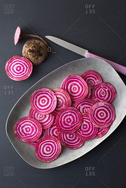 Sliced raw chioggia beets on a platter with a pink knife on slate