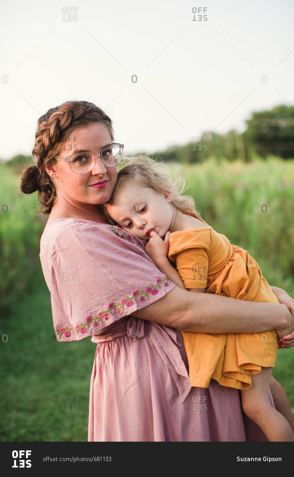 Proud pregnant mom holding sleepy daughter to chest in scenic grassy field