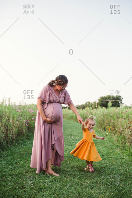 Pregnant mother twirling dancing toddler in field