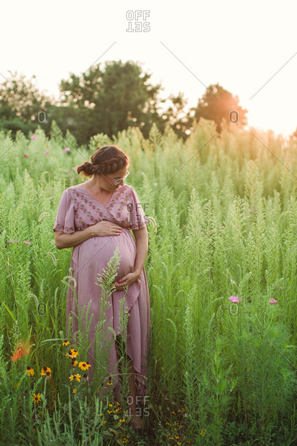 Pregnant mom having peaceful moment in field of tall grass at golden hour