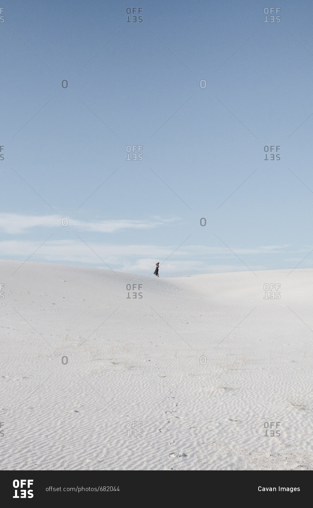 Distant view of woman standing on field against sky at White Sands National Monument