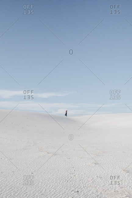 Distant view of woman standing on field against sky at White Sands National Monument