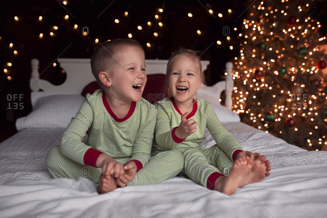 Cheerful siblings sitting on bed against illuminated Christmas Tree at home