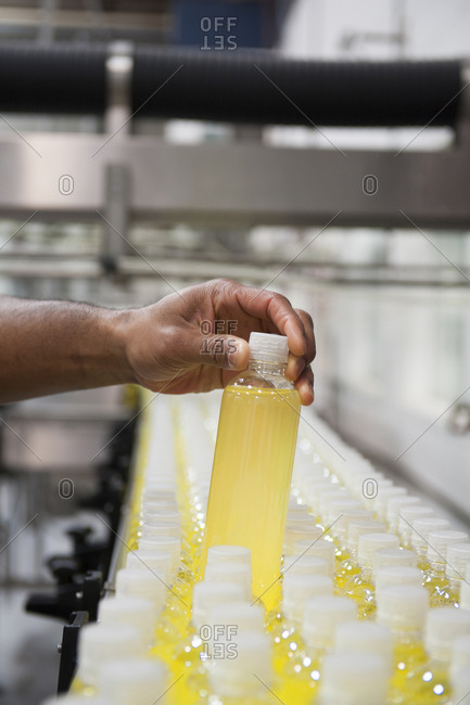 Close-up of a hand checking a bottle of leman flavored water on a production line conveyor belt in a bottling plant.