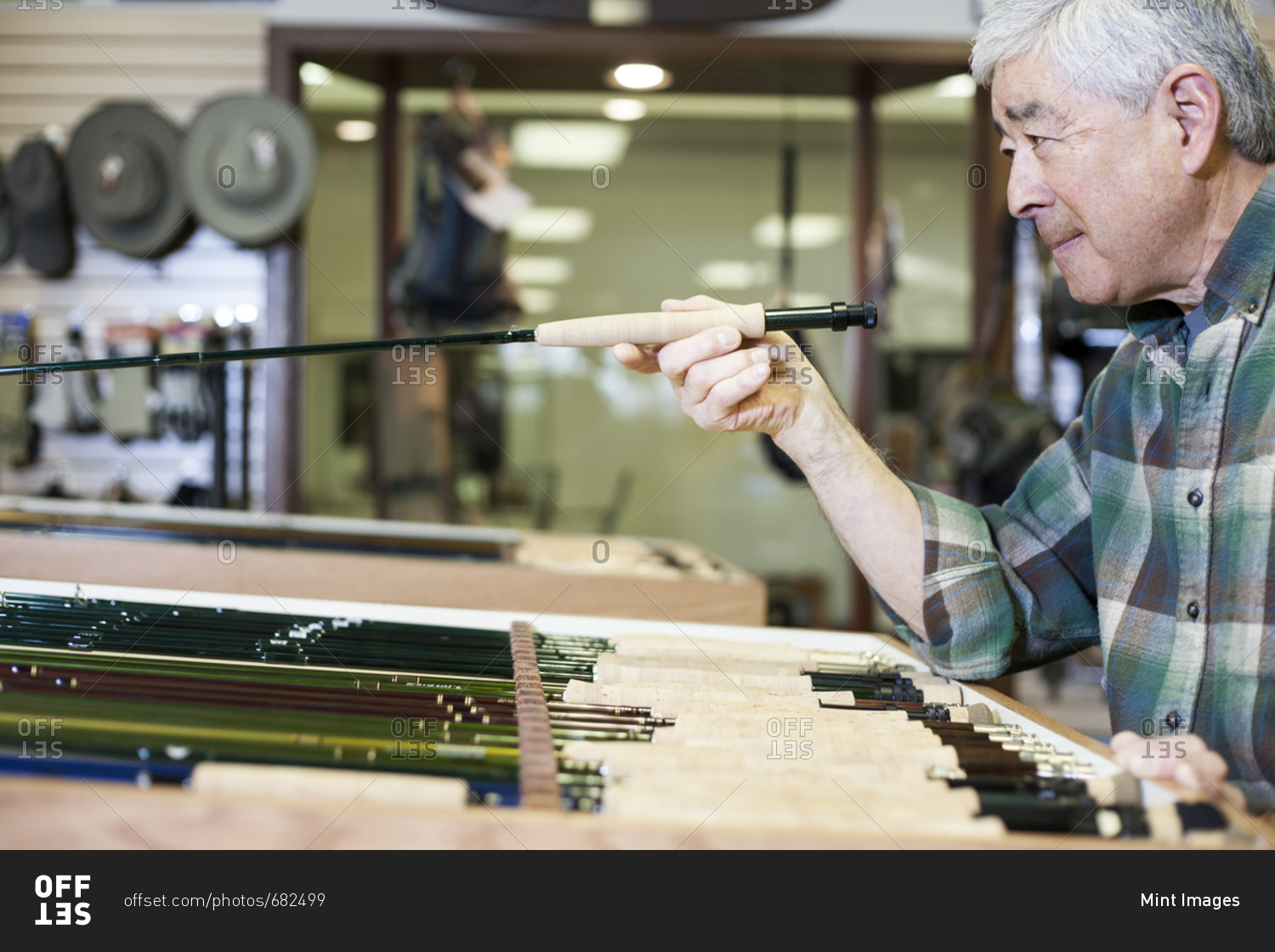 Asian American senior male checking the balance on a 5 weight fly fishing rod for sale in a fly-fishing shop.