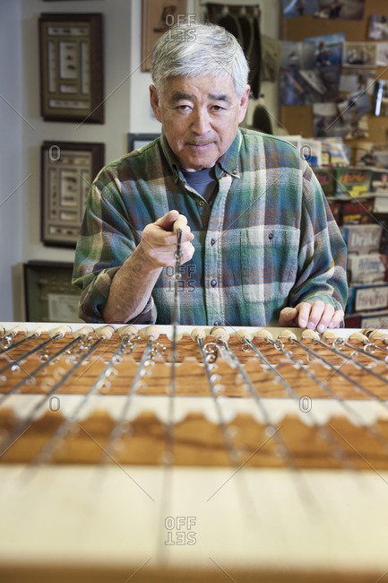 Asian American senior male checking the balance on a 5 weight fly fishing rod for sale in a fly fishing shop.