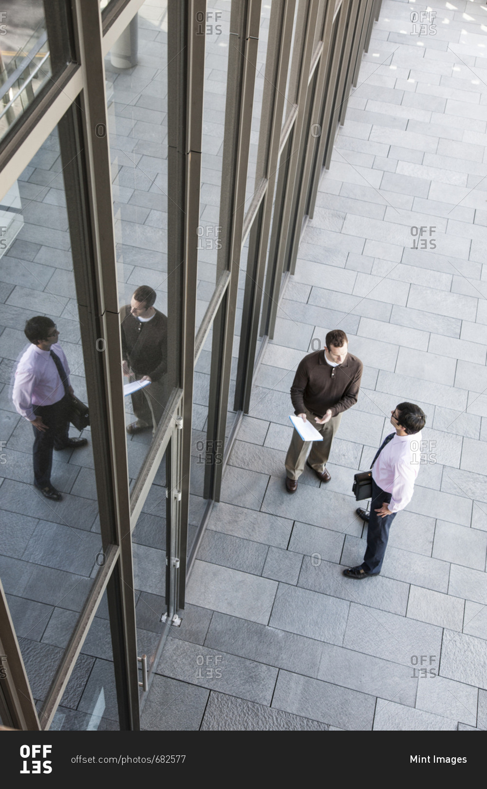 View from above of two businessmen meeting outside of a building next to a bank of windows.