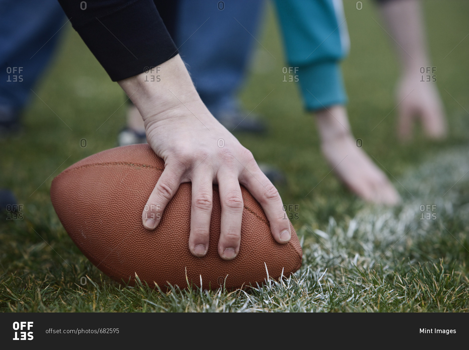 Close up of a hand holding an oval football on the line, during a game of non-contact flag football.
