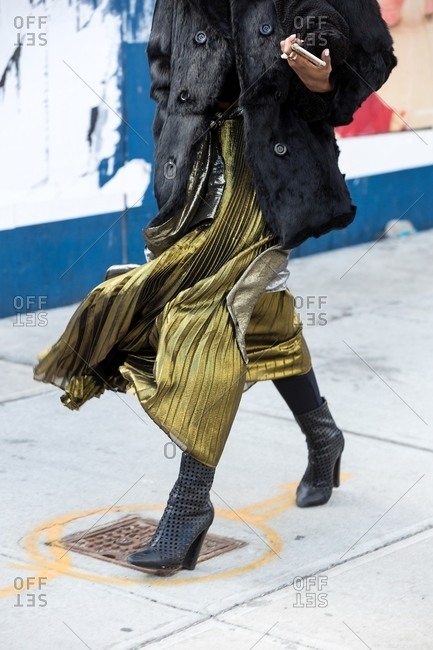 Woman wearing metallic pleated chiffon skirt and faux fur coat striding down the street