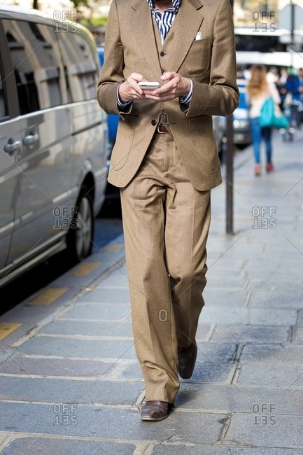 Person walking texting on phone wearing three piece beige suit
